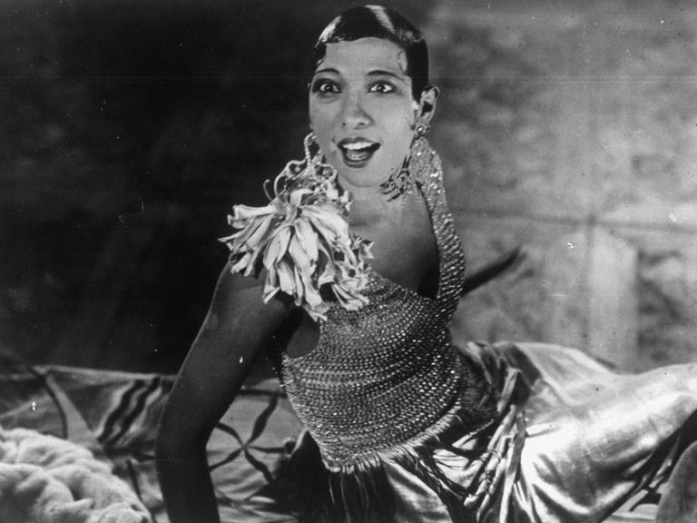 Josephine Baker schaut in ihrem Bühnenoutfit überrascht in die Höhe.