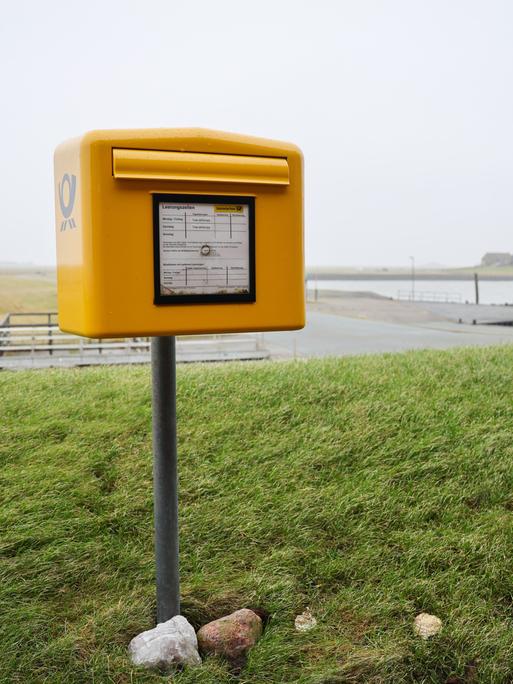Ein Briefkasten der Deutschen Post mit Tide-abhängigen Leerungszeiten steht auf einer Warft auf der Hallig Langeneß.