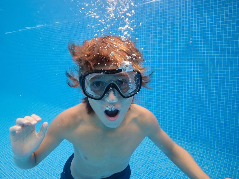 Ein Junge mit Taucherbrille unter Wasser im Pool