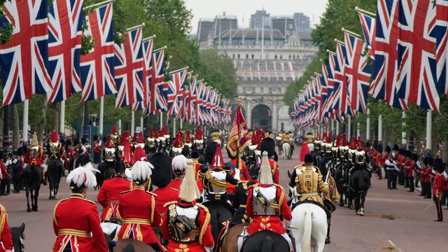 Reiter sitzen in zumeist roten Uniformen auf ihren Pferden. Außerdem sind viele britische Fahnen und Zuschauer zu sehen.