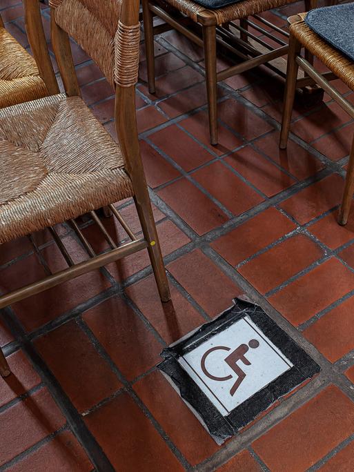 Neben einer Stuhlreihe klebt das Rollstuhlsymbol auf dem Boden in einer Kirche