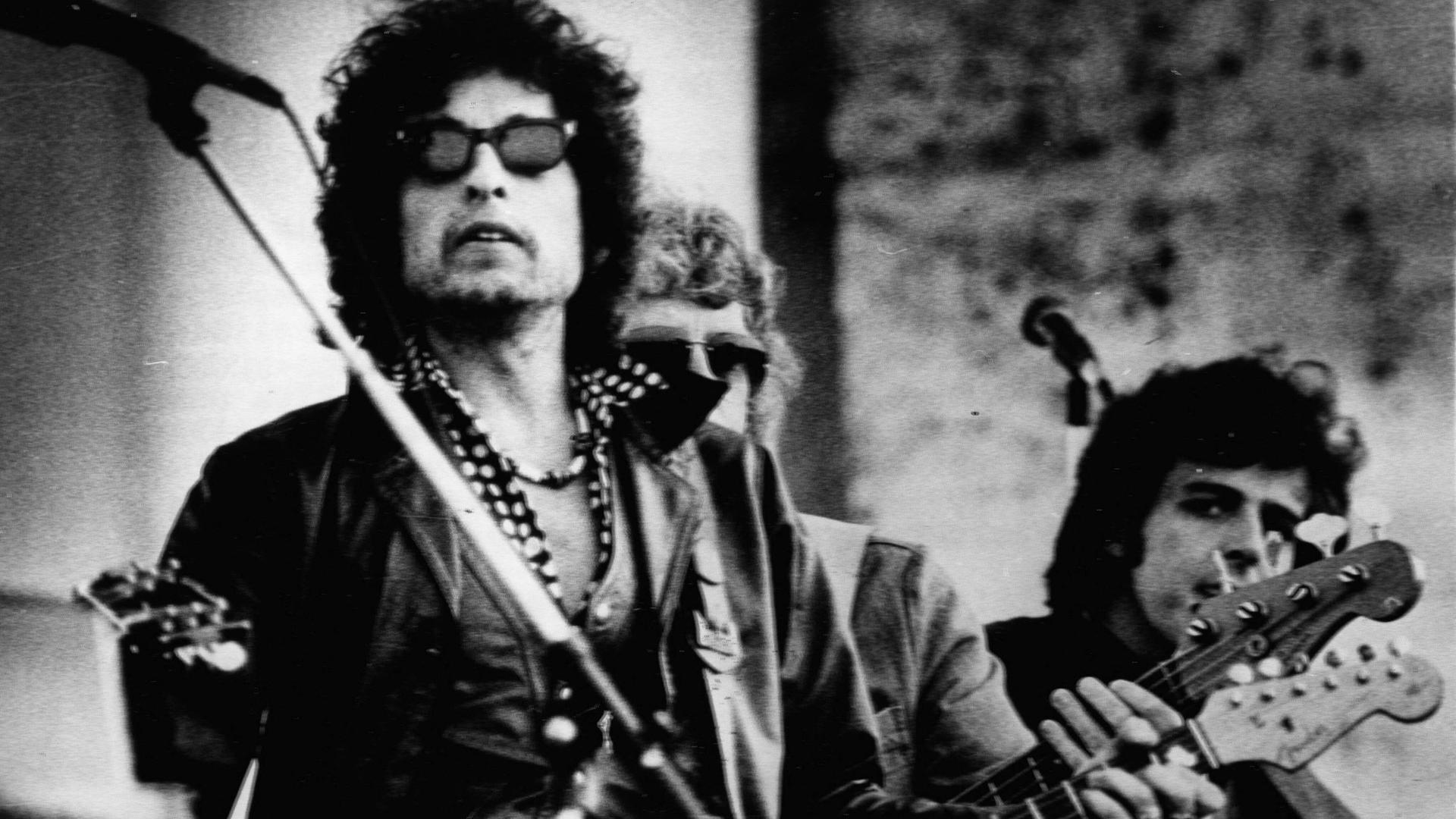 Bob Dylan spielte am 4. Oktober 1975 vor 75.000 Fans in Nürnberg. Im Vordergrund der Sänger mit Sonnenbrille und Gitarre in den Händen, im Hintergrund auf dem Schwarz-Weiß-Bild weitere Musiker. Bob Dylan spielte am 4. Oktober 1975 vor 75.000 Fans in Nürnberg. Im Vordergrund der Sänger mit Sonnenbrille und Gitarre in den Händen, im Hintergrund auf dem Schwarz-Weiß-Bild weitere Musiker.