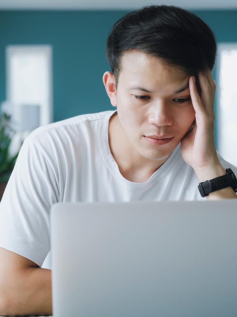 Ein junger Mann sitzt in die Arbeit versunken, den Kopf in eine Hand gestützt an seinem Laptop.