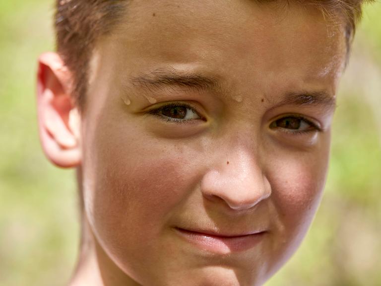 Porträt eines schwitzenden Jungen, die Schweissperlen laufen an seinem Gesicht herunter.