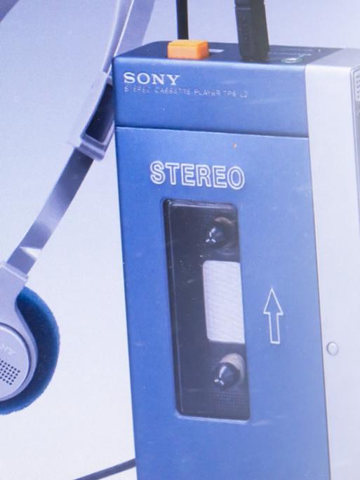 Auf dem Bild ist ein mobiles Kassettenabspielgerät der Firma Sony, ein sogenannter Walkman, zu sehen, daneben der dazugehörige Kopfhörer. 