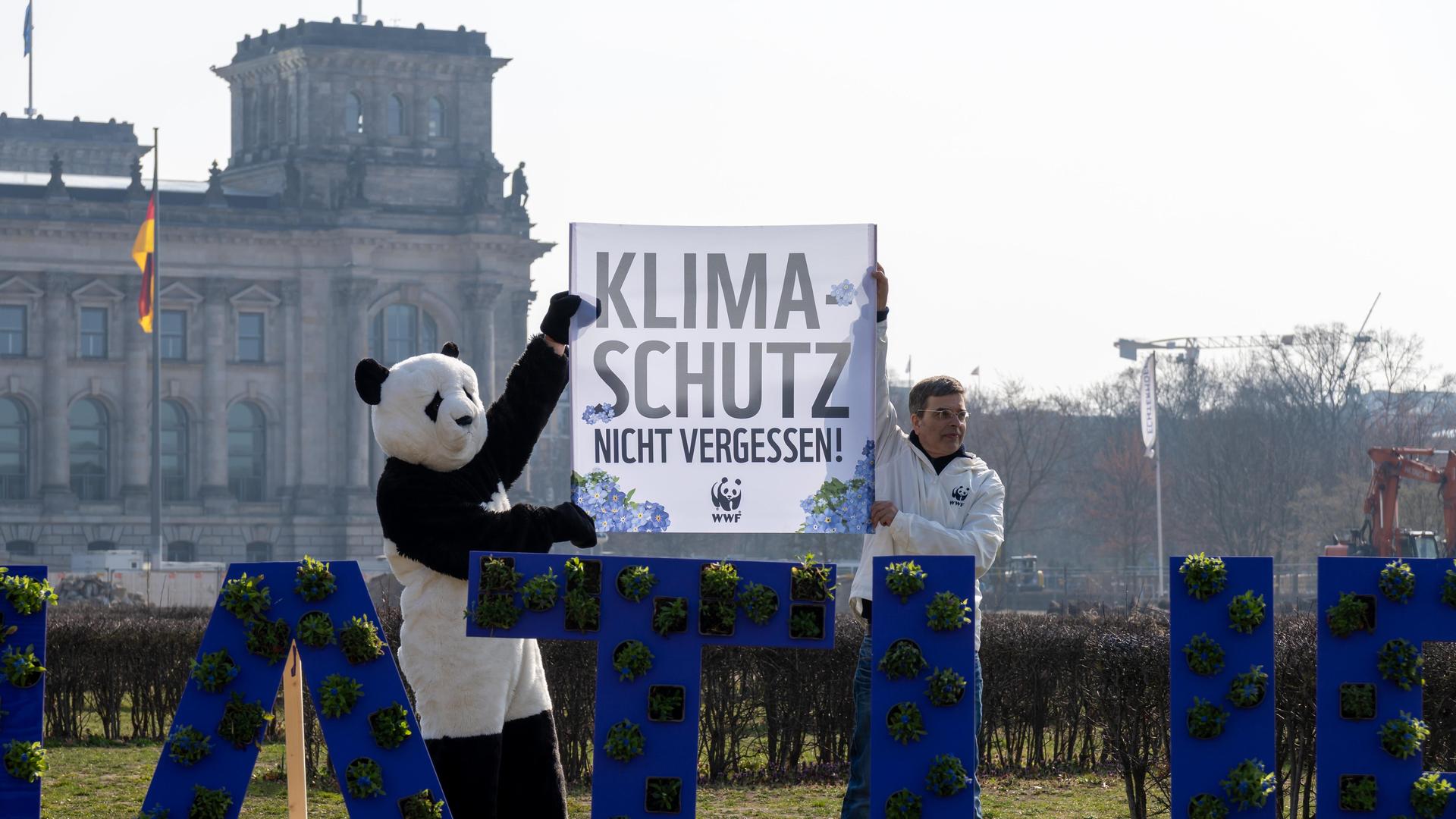 Demonstration der Umweltorganisation World Wide Fund For Nature (WWF) vor dem Reichstagsgebäude in Berlin. Zwei Klimaschützer halten ein Banner hoch mit der Aufschrift: Klimaschutz nicht vergessen. Einer ist als Pandabär verkleidet. 