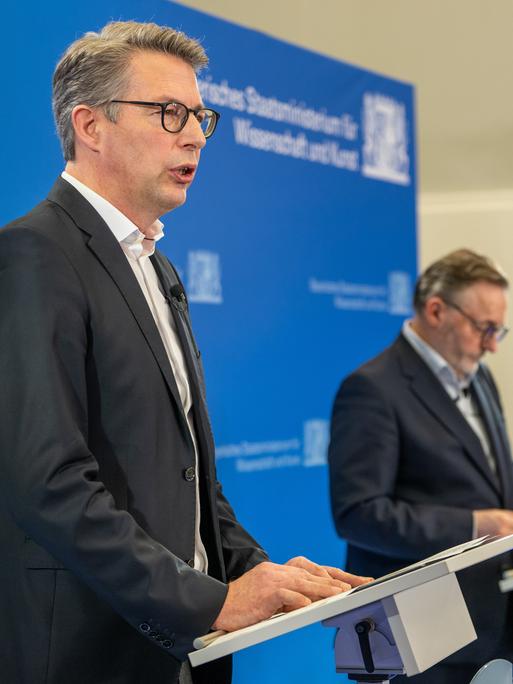 Markus Blume, ein Mann mittleren Alters in dunklem Anzug, spricht bei einer Pressekonferenz ins Mikrofon. Rechts neben ihm steht Anton Biebl, ebenfalls mittleren Alters, ebenfalls im dunklen Anzug und mit ernstem Gesichtsausdruck.