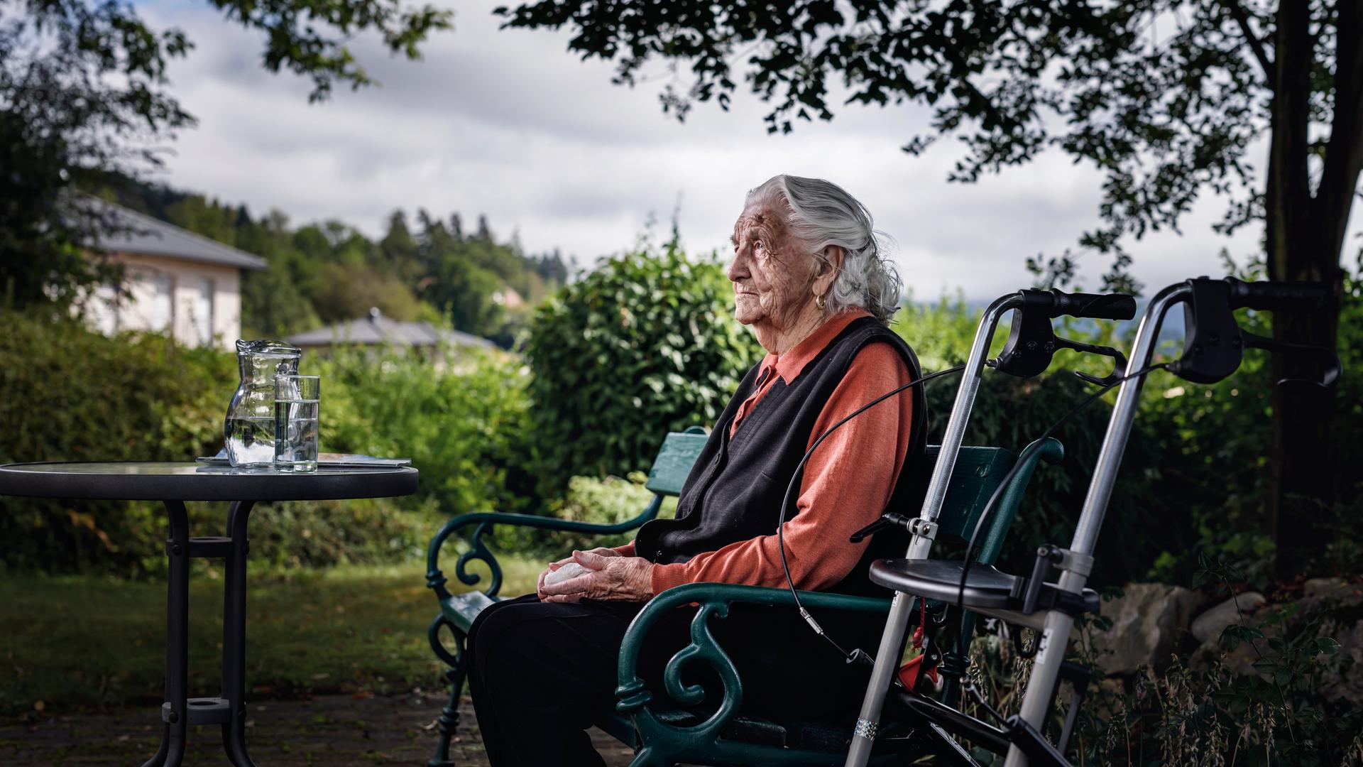 Alte Dame sitzt nachdenklich auf Parkbank, daneben ihr Rollator. Alte Dame sitzt nachdenklich auf Parkbank, daneben ihr Rollator.