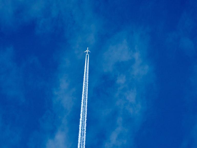 Ein Flugzeug zieht über den Himmel. Hinter ihm sind Kondensstreifen zu sehen.