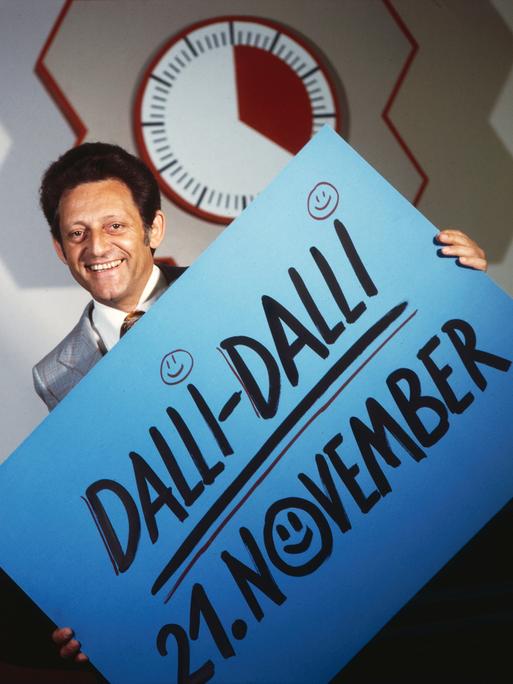 Hans Rosenthal vor der Stoppuhr in der Quiz- und Spielshow "Dalli-Dalli". Er hält ein Schild, auf dem steht: "Dalli Dalli 21. November"