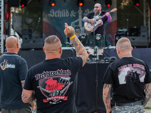 Drei Männer und eine Frau stehen auf dem Areal des Neonazi-Festivals "Schild und Schwert" vor einer Bühne. 