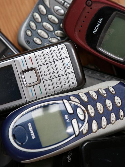 Mehrere ausgediente Mobiltelefone liegen auf einem Tisch.