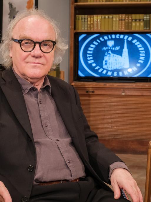 Michael Köhlmeier sitzt in einem Fernsehstudio und blickt in die Kamera.