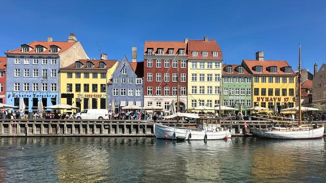 Mehrere bunte Häuser liegen vor einer Bucht. Dort liegen Segel-Schiffe vor Anker. 