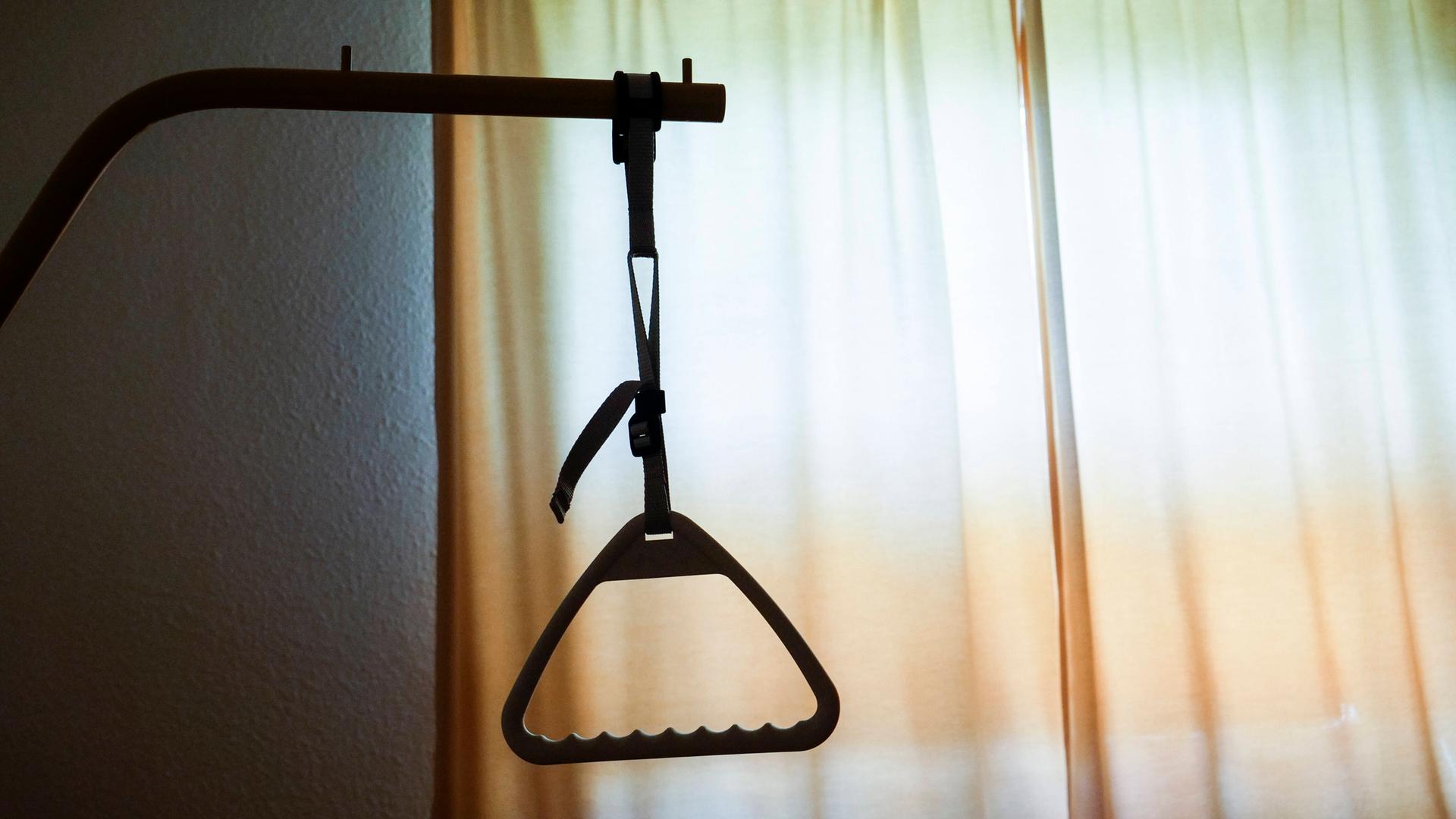 Der Armgriff eines Pflegebettes hebt sich als dunkle Silhouette vor einem Fenster ab. Der Armgriff eines Pflegebettes hebt sich als dunkle Silhouette vor einem Fenster ab.