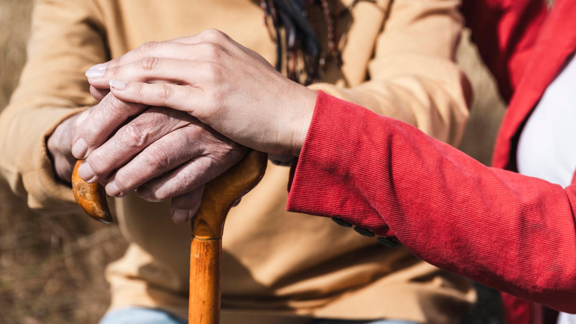 Eine Frau legt ihre Hand auf die eines älteren Herrn. Sie wirken, als wären sie Enkelin und Großvater.